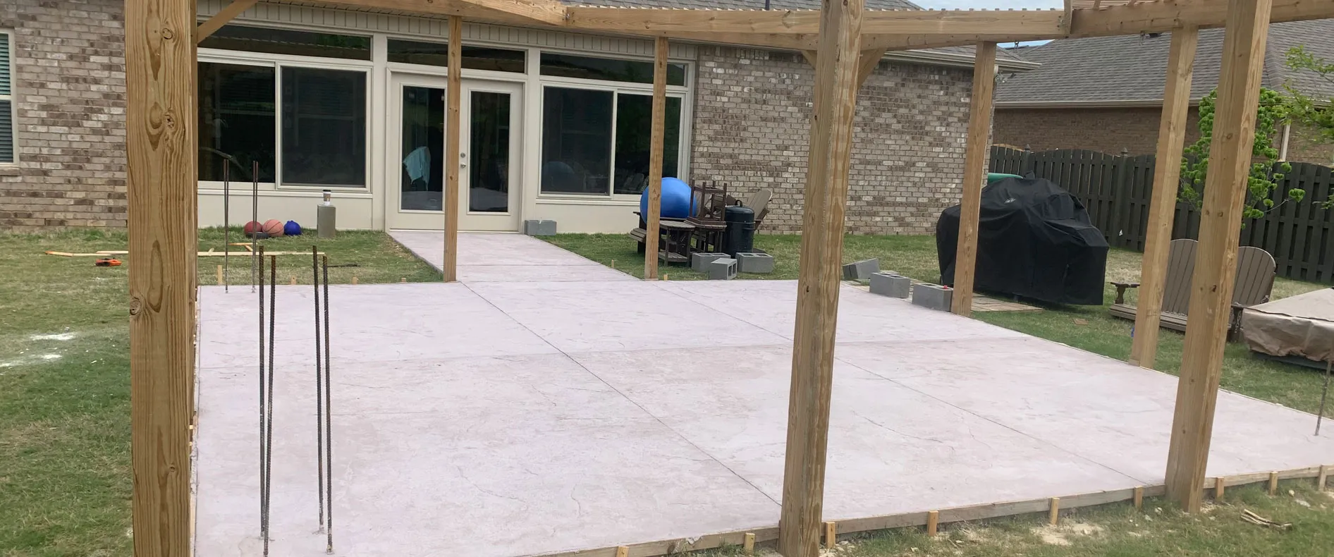 Concrete patio poured beneath a new pergola frame at a brick home in North Alabama