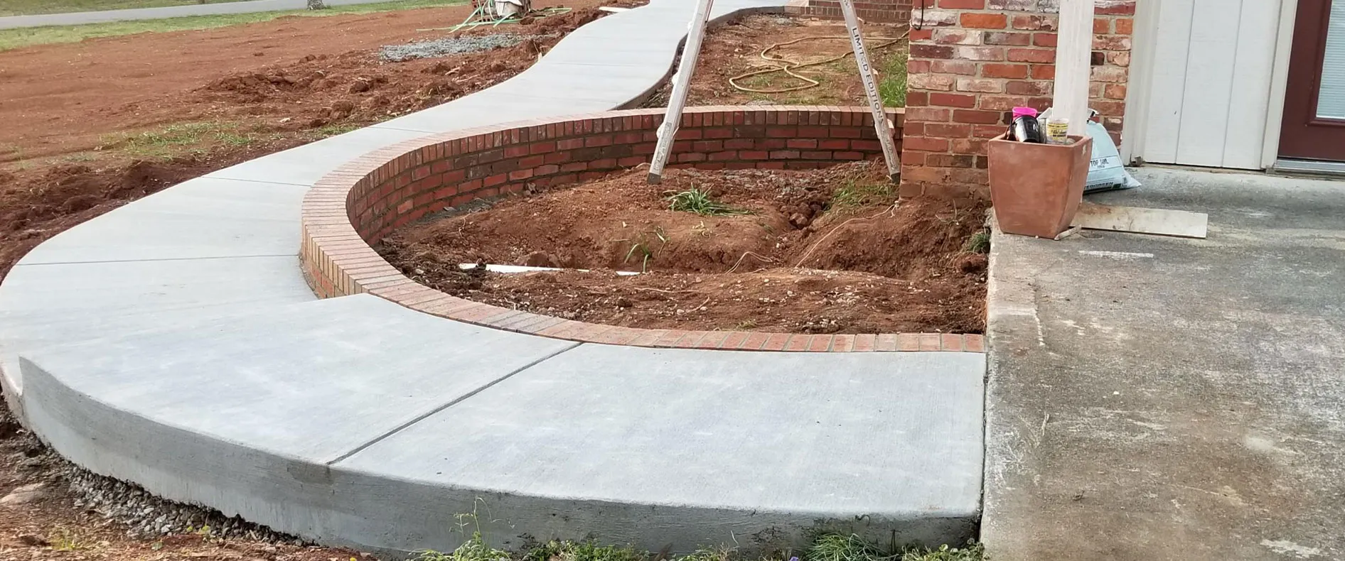 Curved concrete walkway with a brick retaining wall under construction in North Alabama
