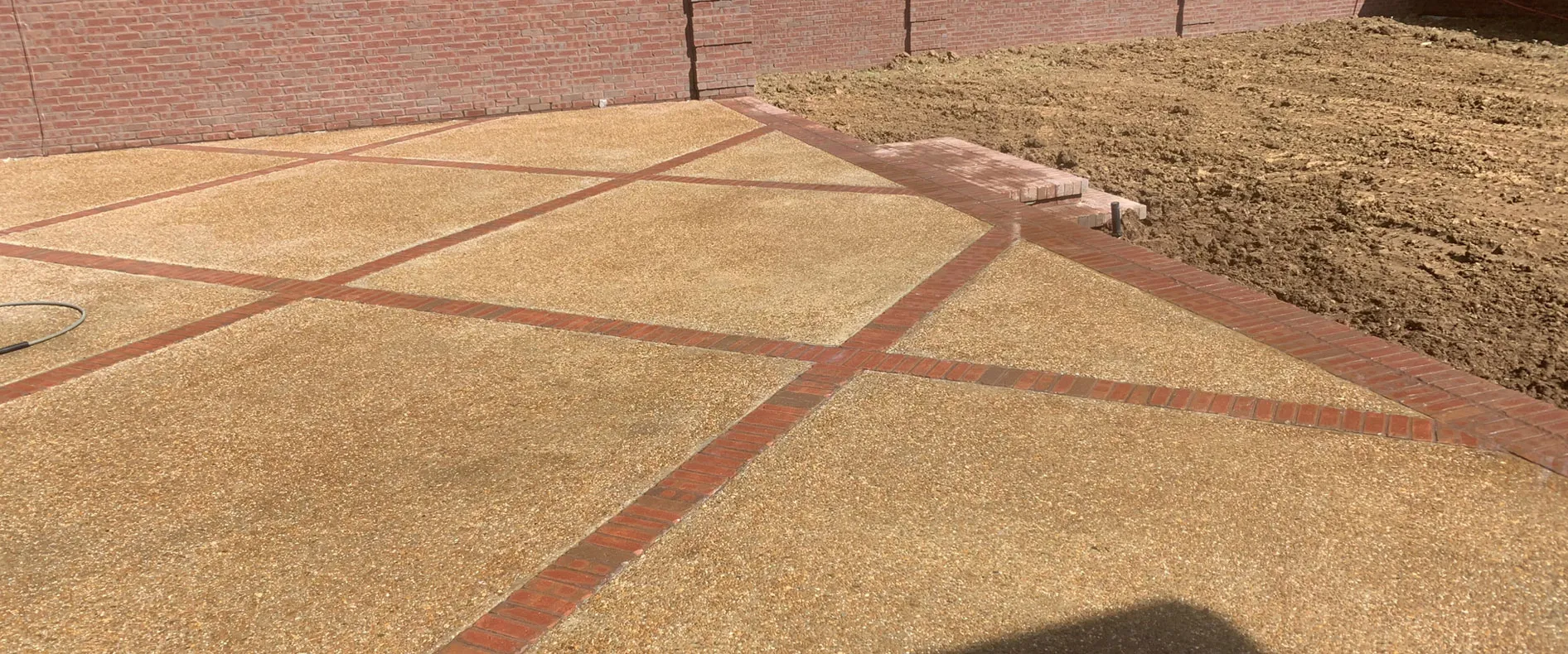 Decorative concrete with red brick banding set into graded ground in North Alabama